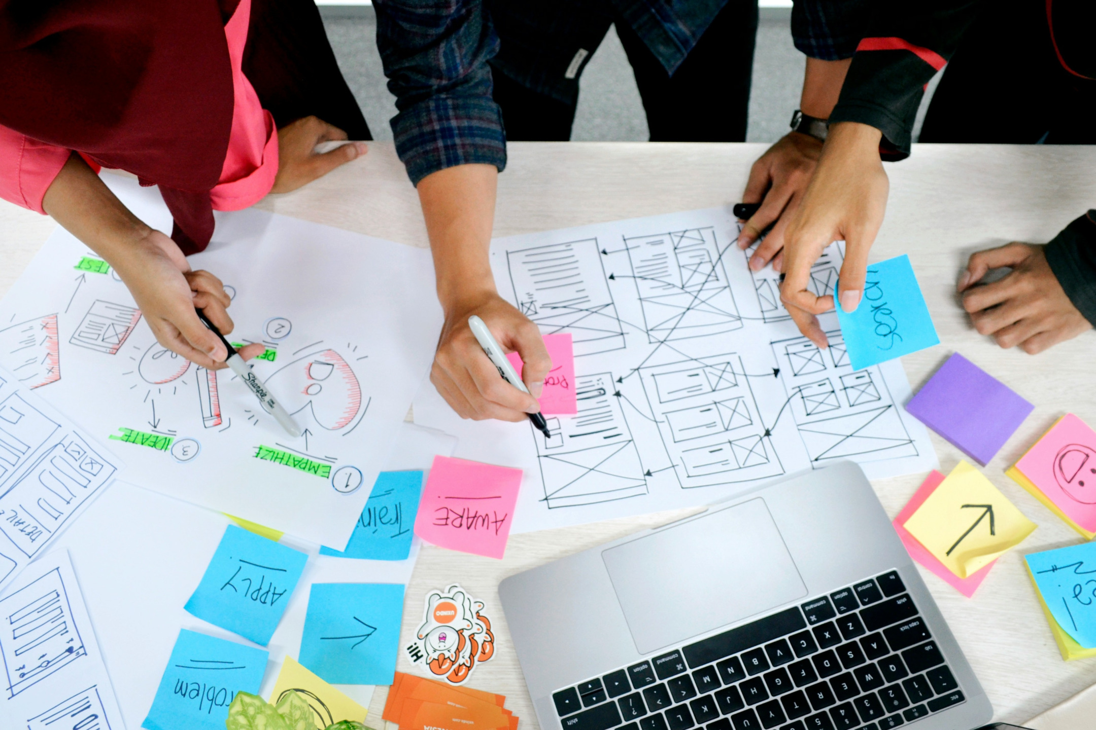 Top down photograph of three people's hands working on planning media projects